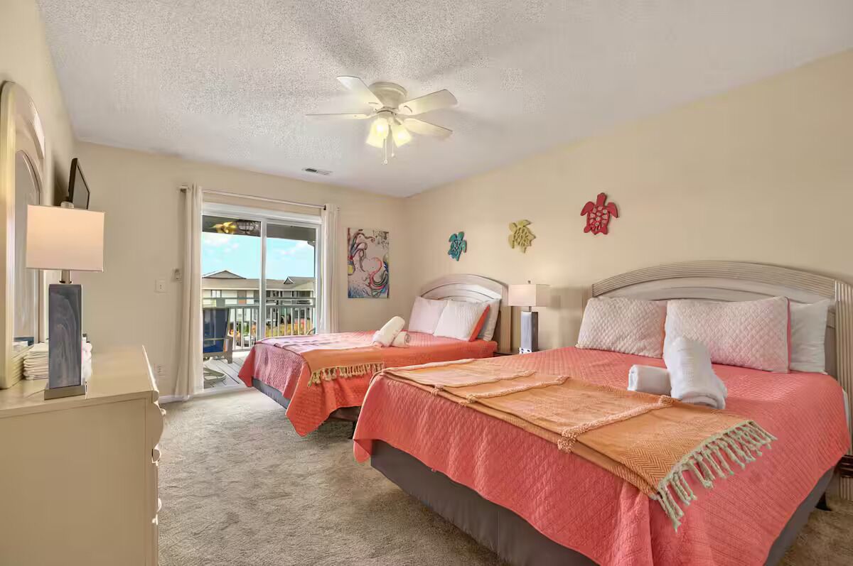 A bedroom with two beds, a ceiling fan, and a view of a balcony.