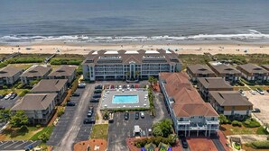 Un hôtel doté d’une piscine centrale, entouré d’un parking et offrant une vue sur la plage.