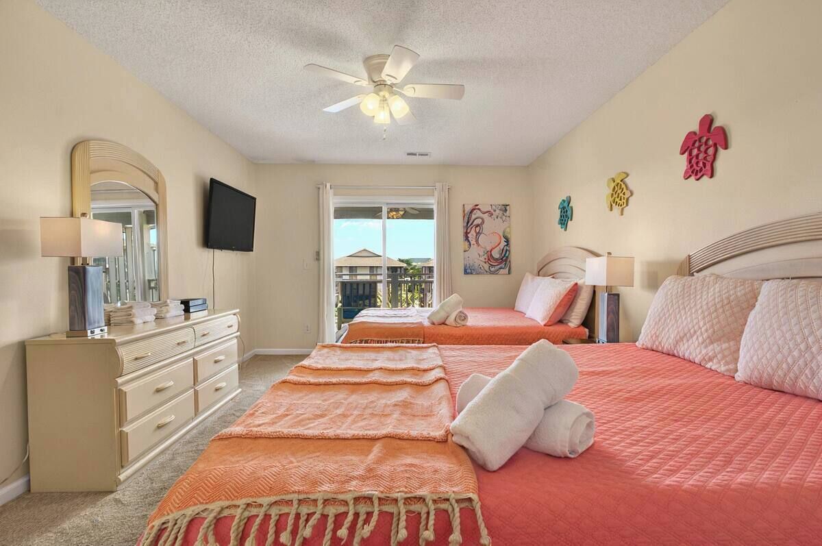 A bedroom with two beds, a ceiling fan, a TV, a dresser, and a window with a view.