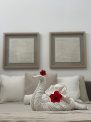 Un lit avec une literie blanche, deux œuvres d’art encadrées accrochées au mur et un cygne décoratif orné d’une fleur rouge.