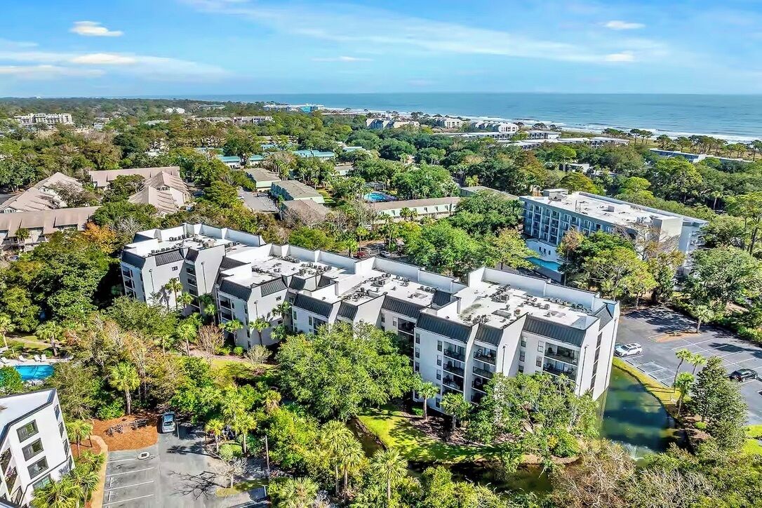 A modern hotel complex with multiple buildings, surrounded by lush greenery and a view of the ocean.