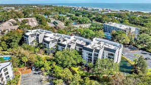 A modern hotel complex with multiple buildings, surrounded by lush greenery and a view of the ocean.