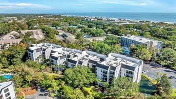 A modern hotel complex with multiple buildings, surrounded by lush greenery and a view of the ocean.