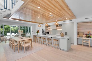 A modern kitchen with a central island, bar stools, and a dining area with wooden chairs.
