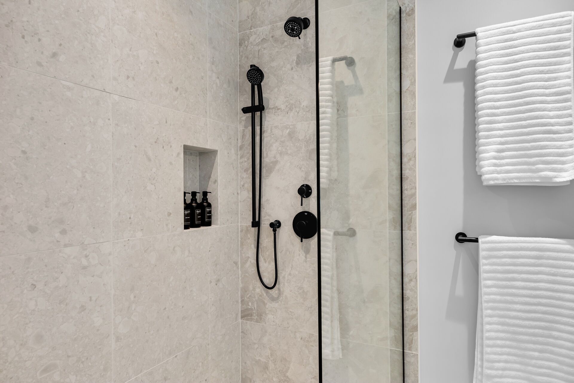 A modern bathroom with a shower, a towel rack, and a shelf with toiletries.