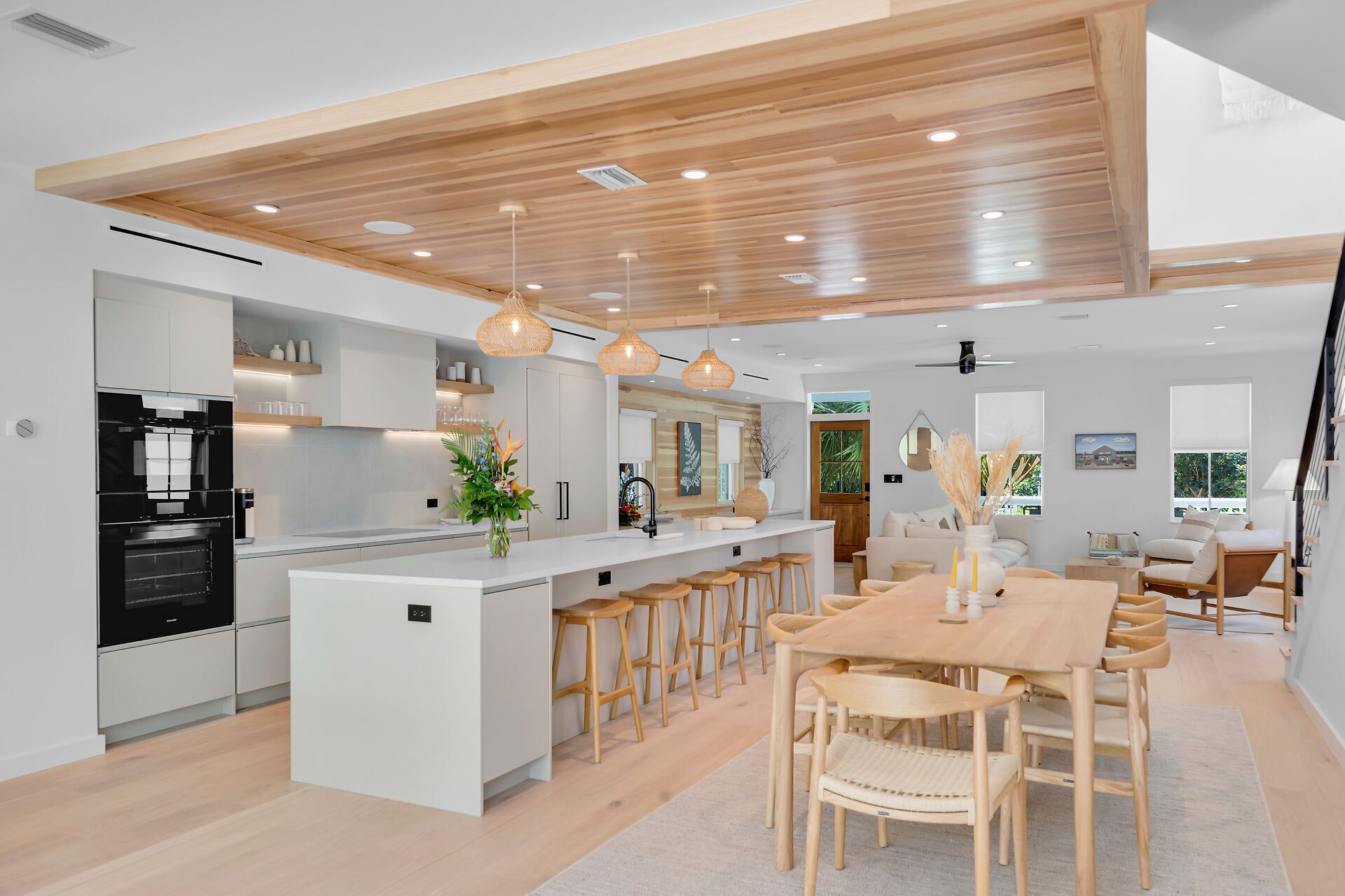 Una cocina moderna con una isla central, taburetes de bar y una zona de comedor con una mesa y sillas de madera.