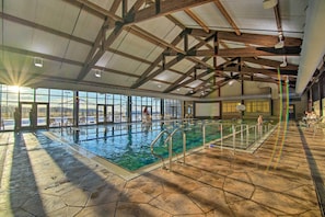 Une piscine intérieure avec des parois en verre transparent, un sol carrelé à motifs hexagonaux et un plafond en bois haut.
