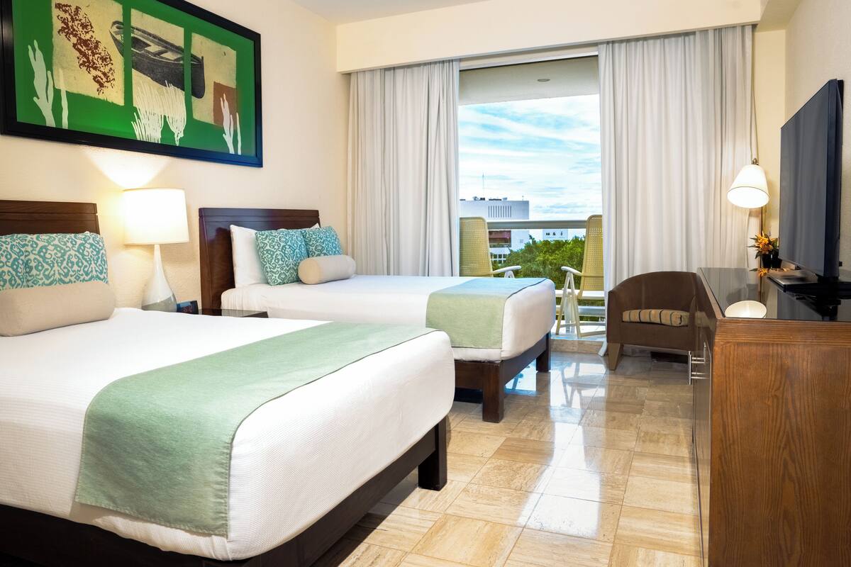 Une chambre d’hôtel avec deux lits, un bureau, une chaise, une télévision et un balcon avec des rideaux.