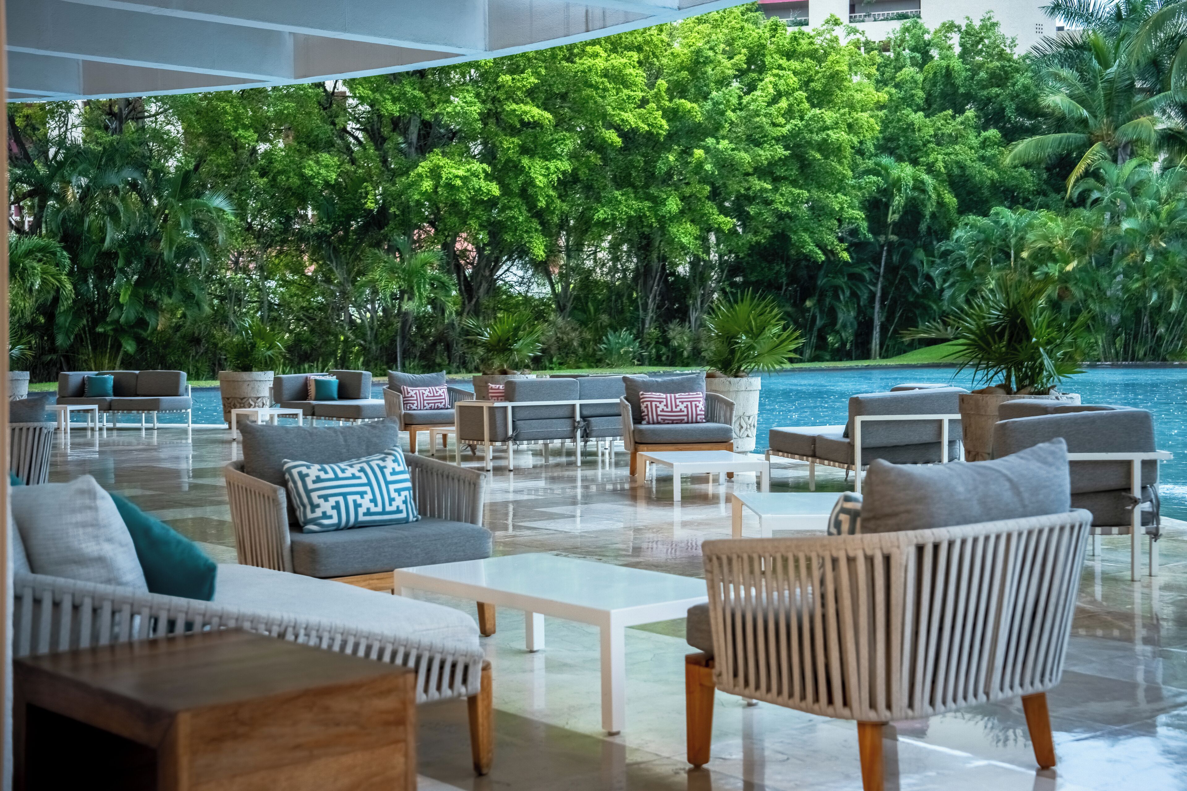 A modern outdoor lounge area with seating arrangements and a view of a pool and lush greenery.
