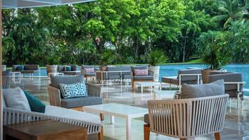 A modern outdoor lounge area with seating arrangements and a view of a pool and lush greenery.