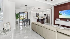 A modern kitchen with white cabinets, a dining area with a table and chairs, and a large TV on the wall.
