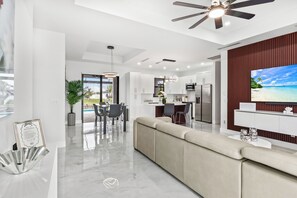 A modern kitchen with white cabinets, a dining area with a table and chairs, and a large TV on the wall.