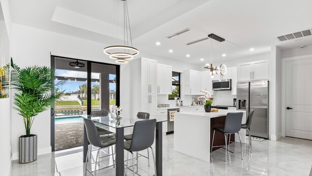 A modern kitchen with white cabinets, a stainless steel refrigerator, and a glass dining table with chairs.