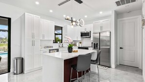 A modern kitchen with white cabinets, a central island with bar stools, stainless steel appliances, and a hanging light fixture.