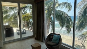 Una stanza con un'ampia porta scorrevole in vetro che dà su un balcone con vista sulla spiaggia e sulle palme.