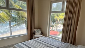 Una camera da letto con un letto, una sedia e ampie finestre vista spiaggia.