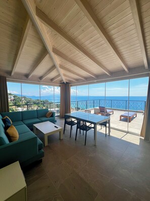 A spacious room with a high ceiling, a large window overlooking a scenic view, a sofa, a table, and chairs.