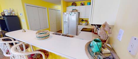 A compact kitchen with white cabinets, a refrigerator, and a dining area with a white table and chairs.