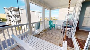 A wooden deck with white railings, a turquoise chair, and a white bench. - South Beach Ocean S by Tybee Vacation Rentals (Tybee Island)