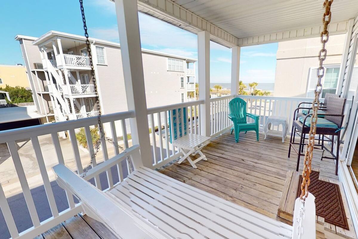 A wooden deck with white railings, a turquoise chair, and a white bench.