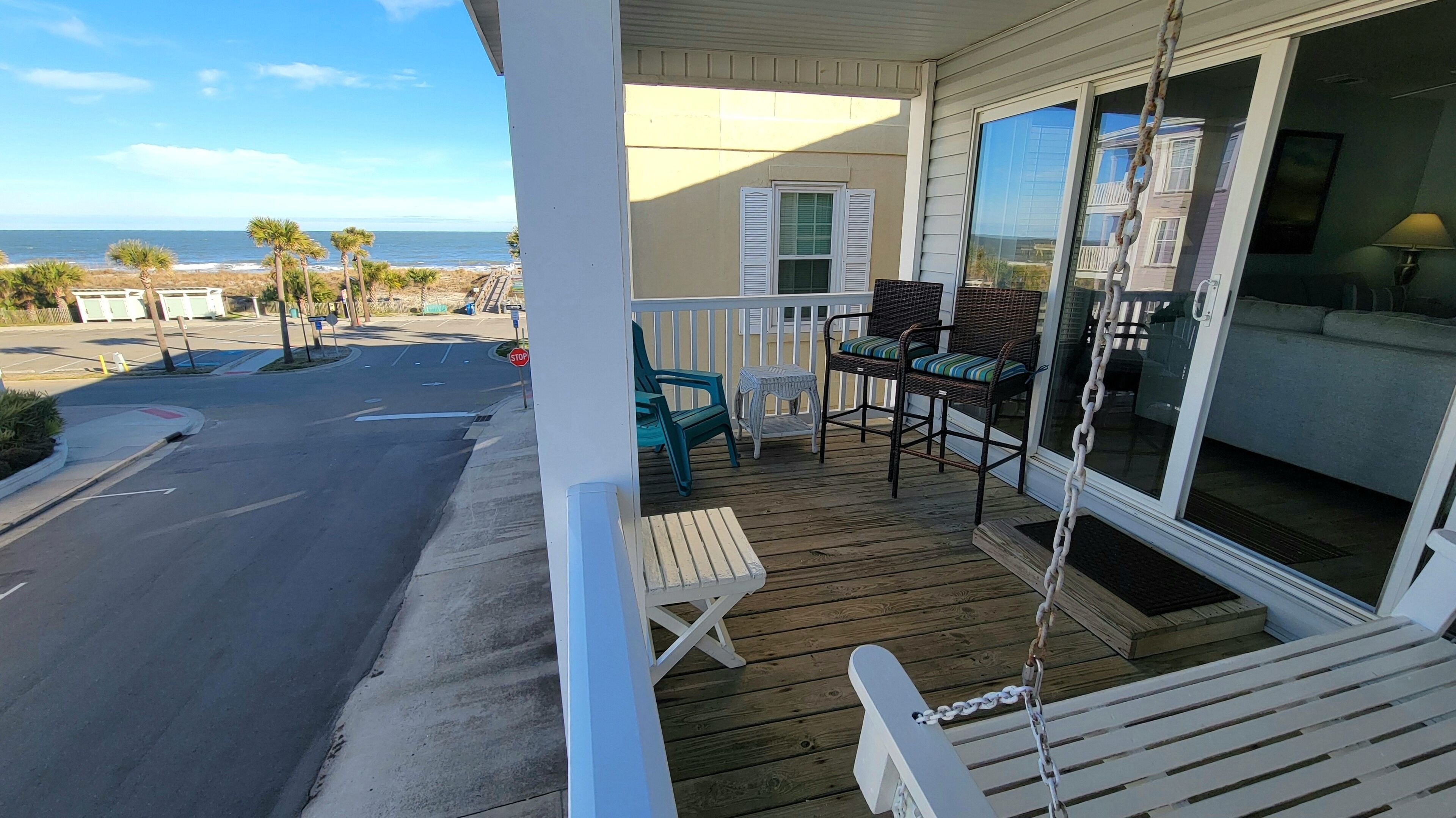 A wooden deck with outdoor furniture, a view of the ocean, and a building with large windows.