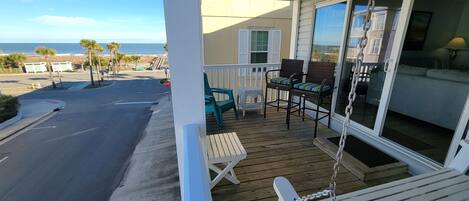 A wooden deck with outdoor furniture, a view of the ocean, and a building with large windows.