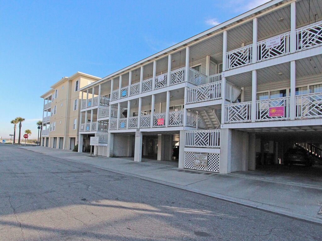 A beachfront hotel with multiple balconies, a covered parking area, and a clear sky.