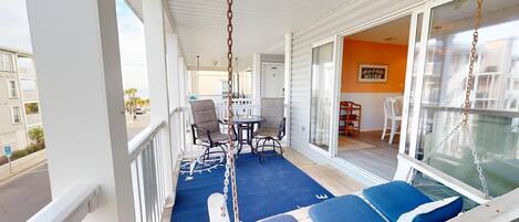 A balcony with a swing chair, a table with chairs, and a view of the street.