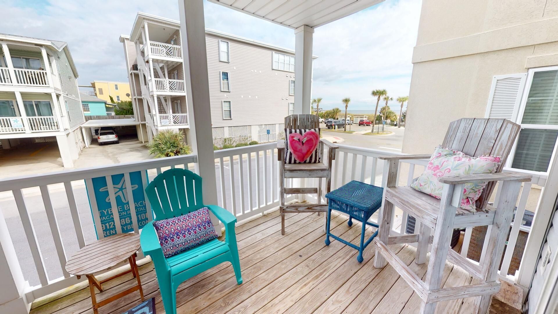 A wooden deck with two chairs and a small table, overlooking a street with buildings and a clear sky.