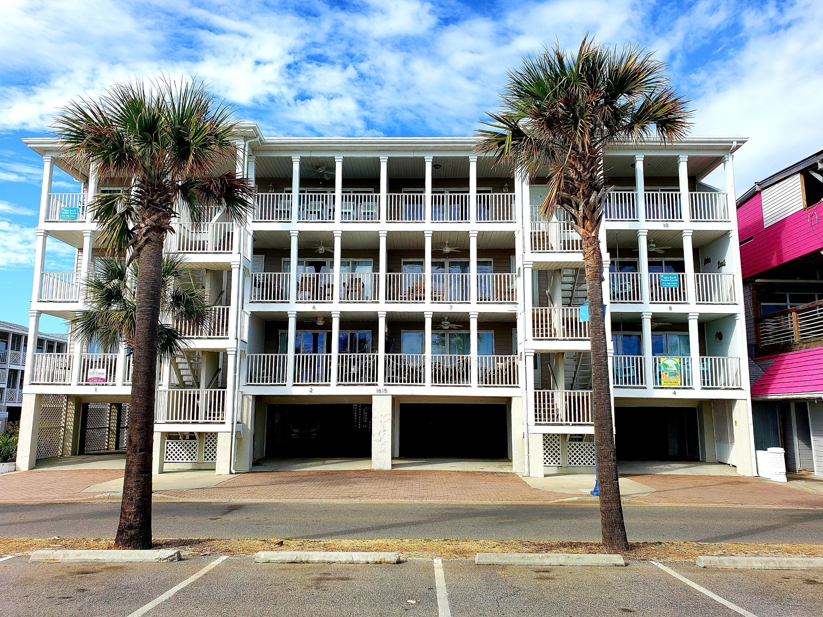 A multi-story hotel with balconies, a covered parking area, and palm trees.