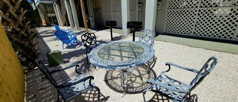 Un área de estar al aire libre con una mesa redonda y cuatro sillas, rodeada por un suelo de grava y un cerramiento de celosía.