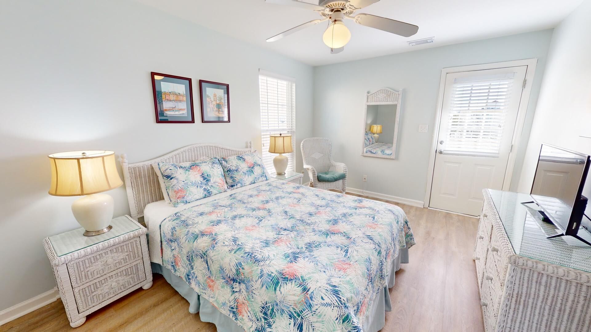 Une chambre à coucher comprenant un lit, des tables de chevet, une chaise, un bureau, un ventilateur de plafond et deux tableaux encadrés accrochés au mur.