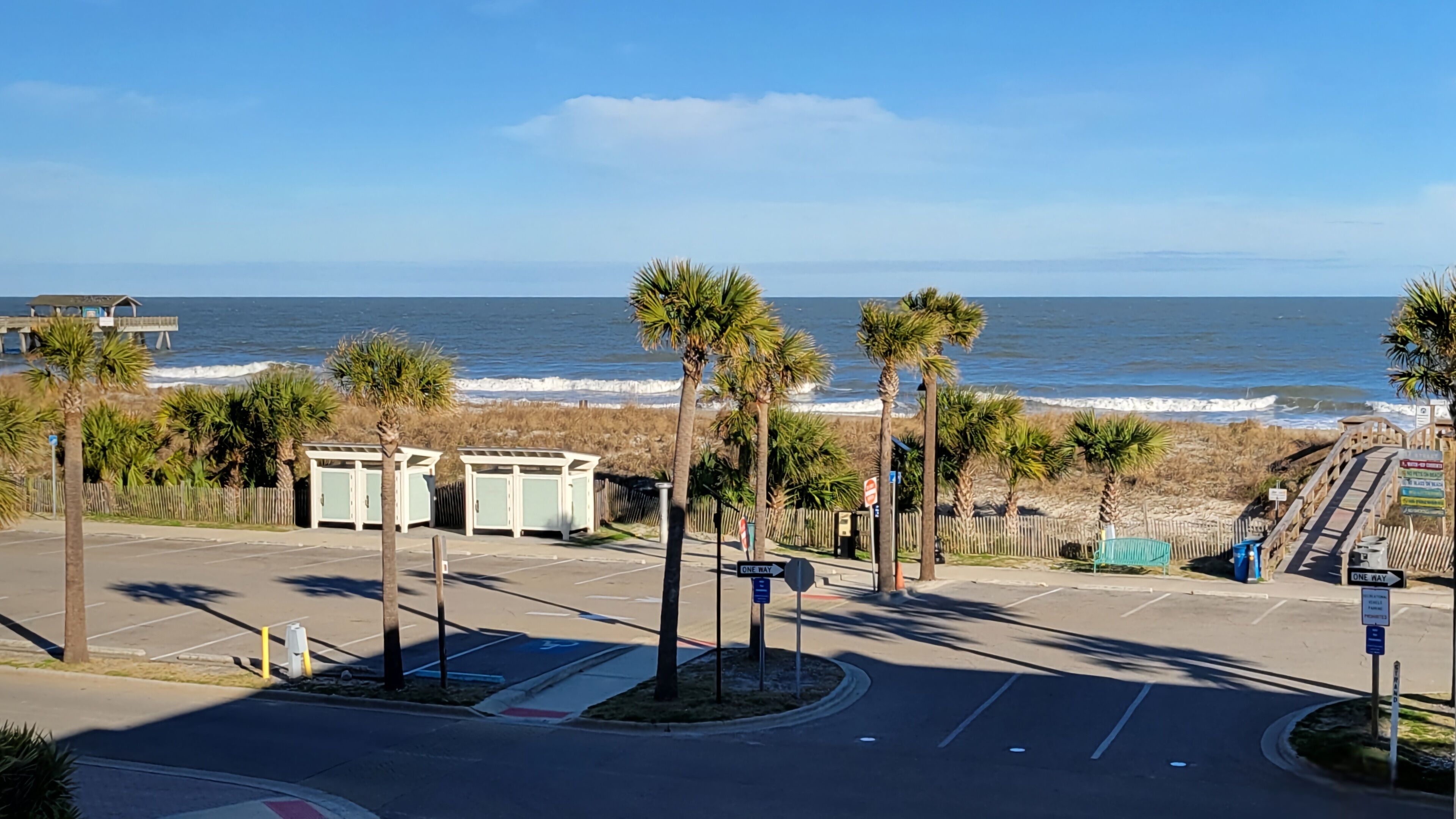 Un estacionamiento con vista al océano, palmeras y un muelle de madera.