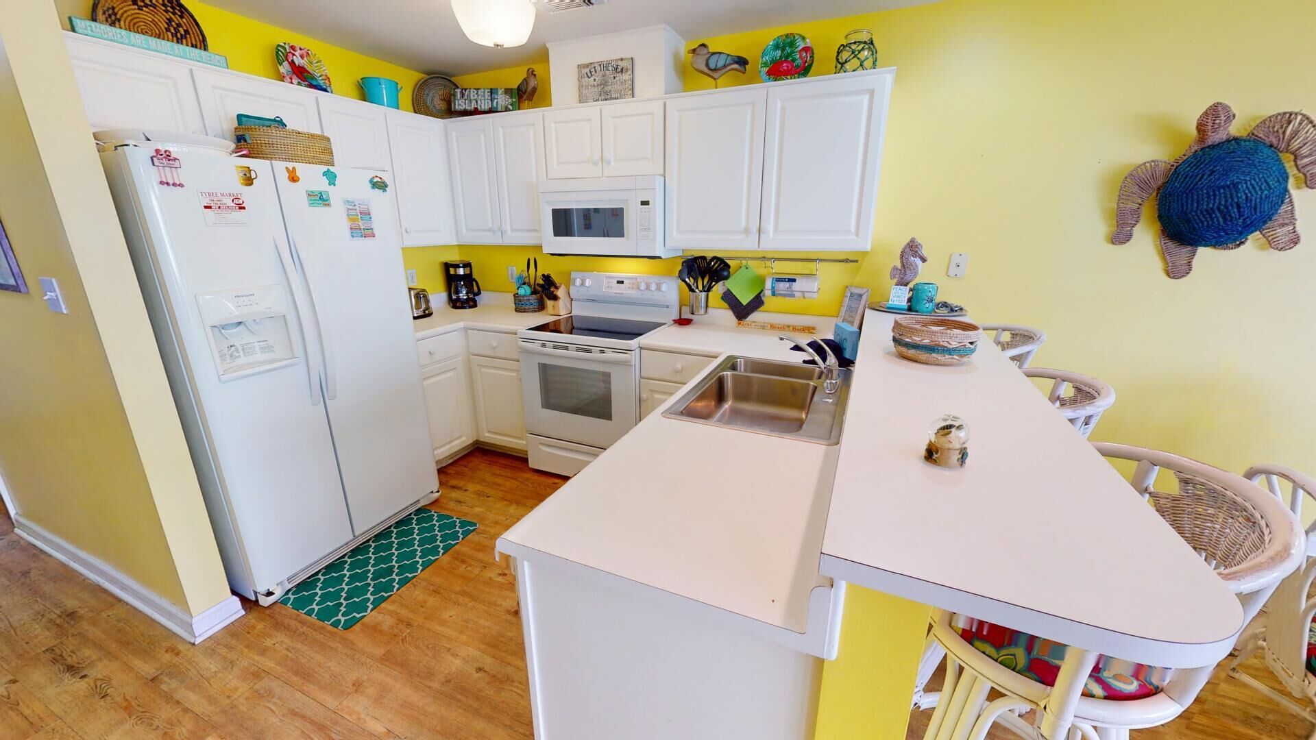 A compact kitchen with white cabinets, a microwave, a stove, and a sink. There are decorative items on the walls and a small island with a sink.