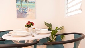 A dining area with a round table set for four, surrounded by teal chairs. There is a painting of a beach scene on the wall behind the table. - Casa Paloma「UNIT 2 「Judith」Walk to beach (San Juan)