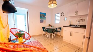 A compact kitchen with white cabinets, a dining area with a round table and chairs, and a bright, open space with a door leading outside. - Casa Paloma「UNIT 2 「Judith」Walk to beach (San Juan)