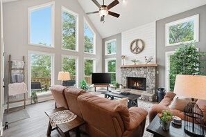 A spacious living room with a stone fireplace, large windows, and a television.