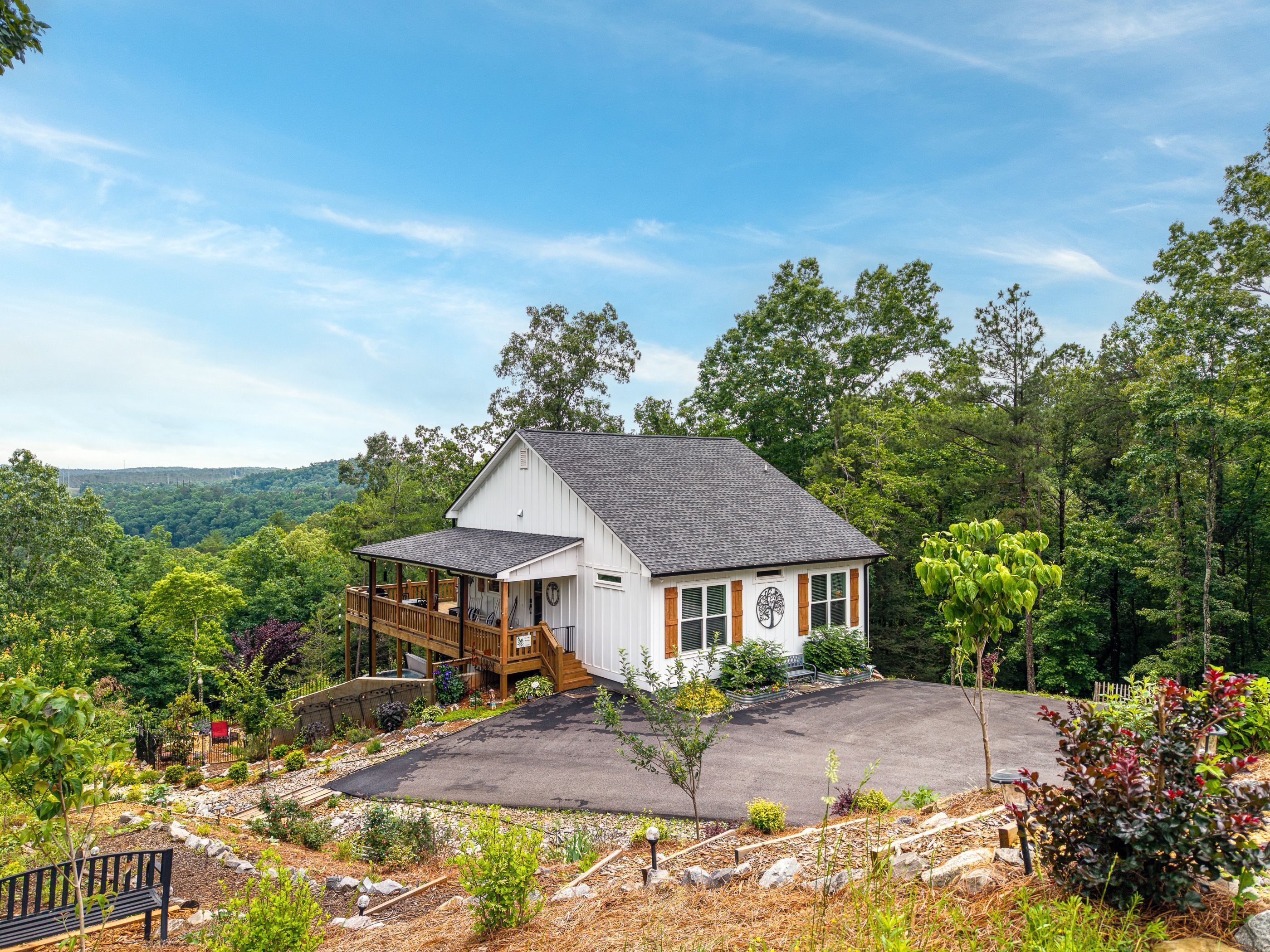 A two-story house with a porch, surrounded by a landscaped garden and a view of a forested area.