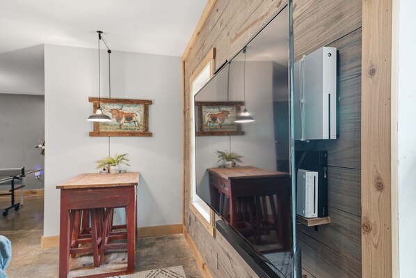 A room with a wooden wall, a large mirror, a wooden table with a plant, and a mounted TV. - Mountain Escape with Hot Tub | Game Room | Trails (Ellijay)