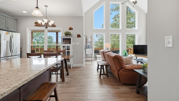 A spacious kitchen with a large island, wooden flooring, and a view of the outdoors through large windows.