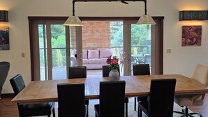 A dining area with a wooden table and chairs, a vase of flowers, and a view of a patio with a sofa.