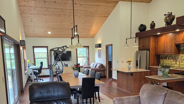 A spacious living area with a high ceiling, wooden flooring, and a kitchen area with wooden cabinets and a refrigerator.