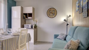 A modern living room with a teal sofa, a dining table set with white plates and glasses, a white refrigerator, and a wall clock. - SGHouse apartment with free parking (Rivoli)