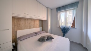 A bedroom with a bed, a wooden headboard, white cabinets, and a window with sheer curtains. - SGHouse apartment with free parking (Rivoli)