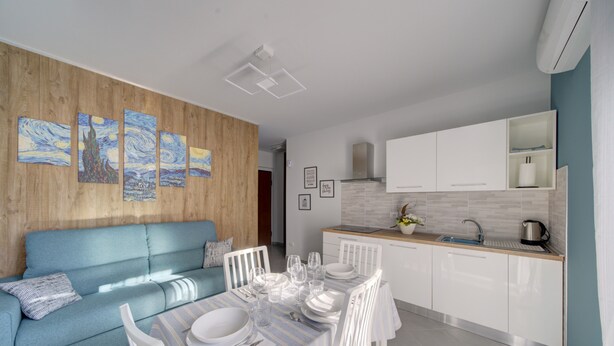 A modern kitchen with white cabinets, a dining area with a striped tablecloth, and a blue sofa. - SGHouse apartment with free parking (Rivoli)