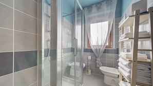 A bathroom with a glass shower enclosure, a toilet, a bidet, and a shelf with folded towels. - SGHouse apartment with free parking (Rivoli)