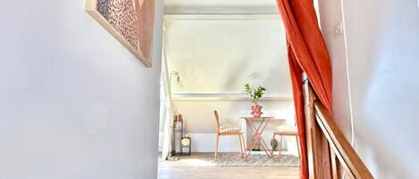 Een trap leidt naar een eetgedeelte met een tafel en stoelen, een hangende ventilator en een schilderij aan de muur.