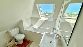Une salle de bain moderne dotée d’une lucarne, d’une baignoire, de toilettes et d’un lavabo.