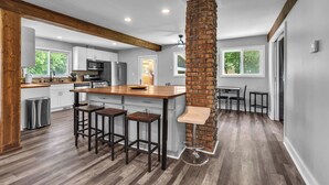 A modern kitchen with a central island, wooden bar stools, and a brick accent wall.