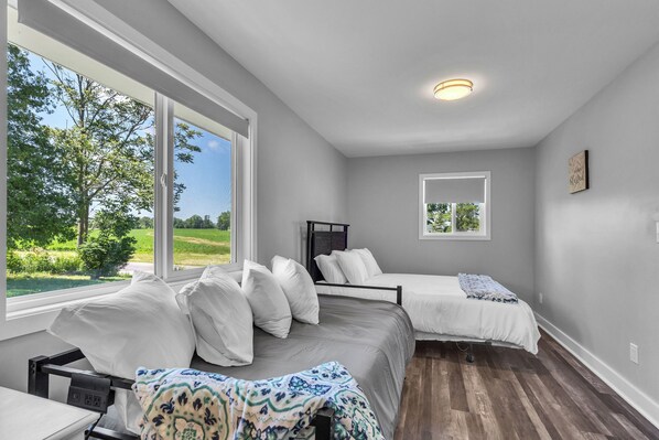 Une chambre avec deux lits, de grandes fenêtres, un luminaire au plafond et une vue sur la verdure.